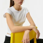 Young woman sitting on a yellow chair wearing white top and black pants