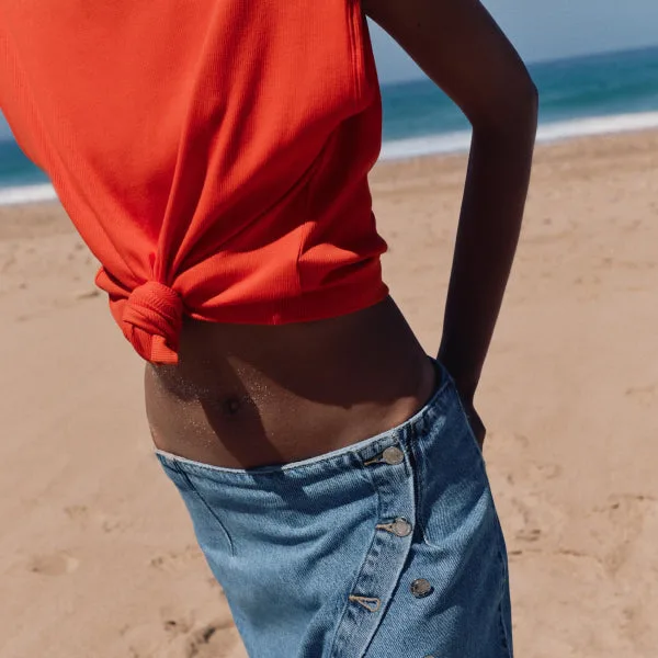 woman wearing orange tied top and jeans on beach